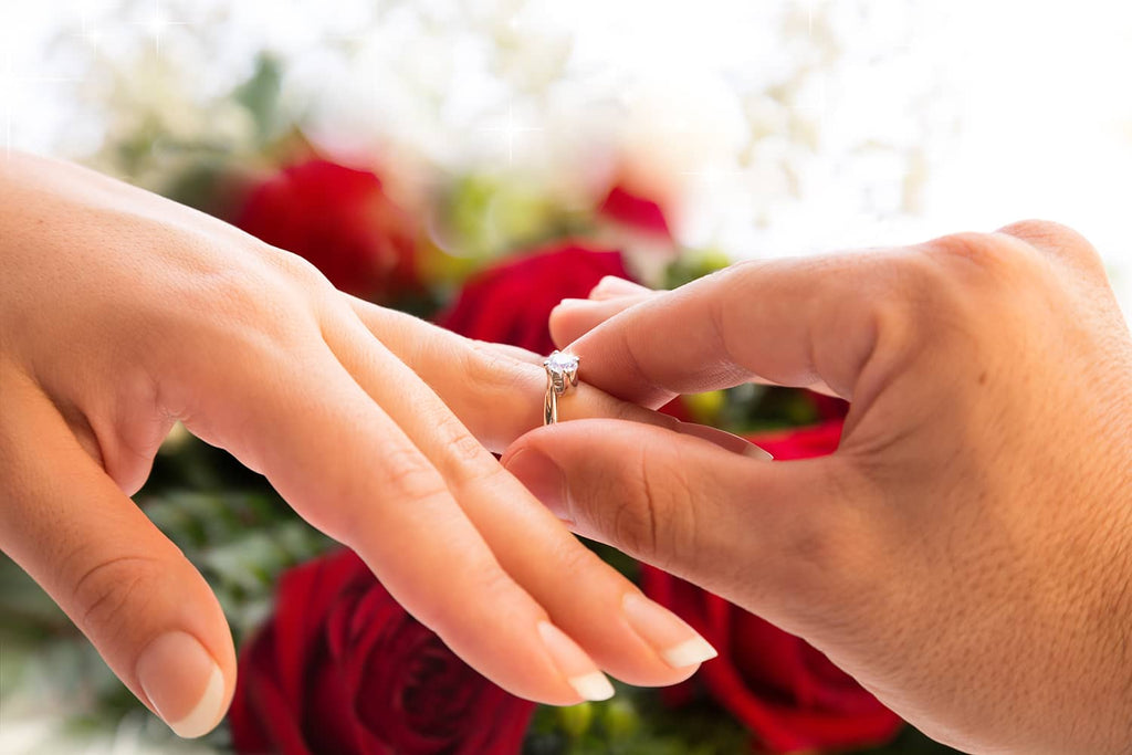 Close up photograph of one person's hand putting an engagement ring on to another person's hand